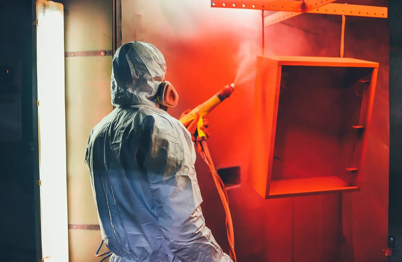 Mitarbeiter trägt Pulverlack auf Metallgehäuse auf – Schutzanzug und Atemmaske